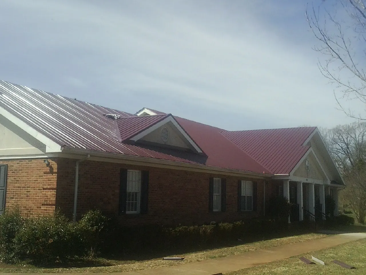 Red metal roof with gabled entries on a long brick building, from a Hail Damage Roof Repair job in Fitzwilliam