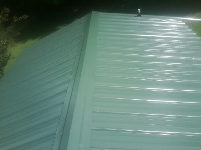 New green metal panels meeting at the ridge of a roof — Flat Roof Repair work by our crew in Fitzwilliam