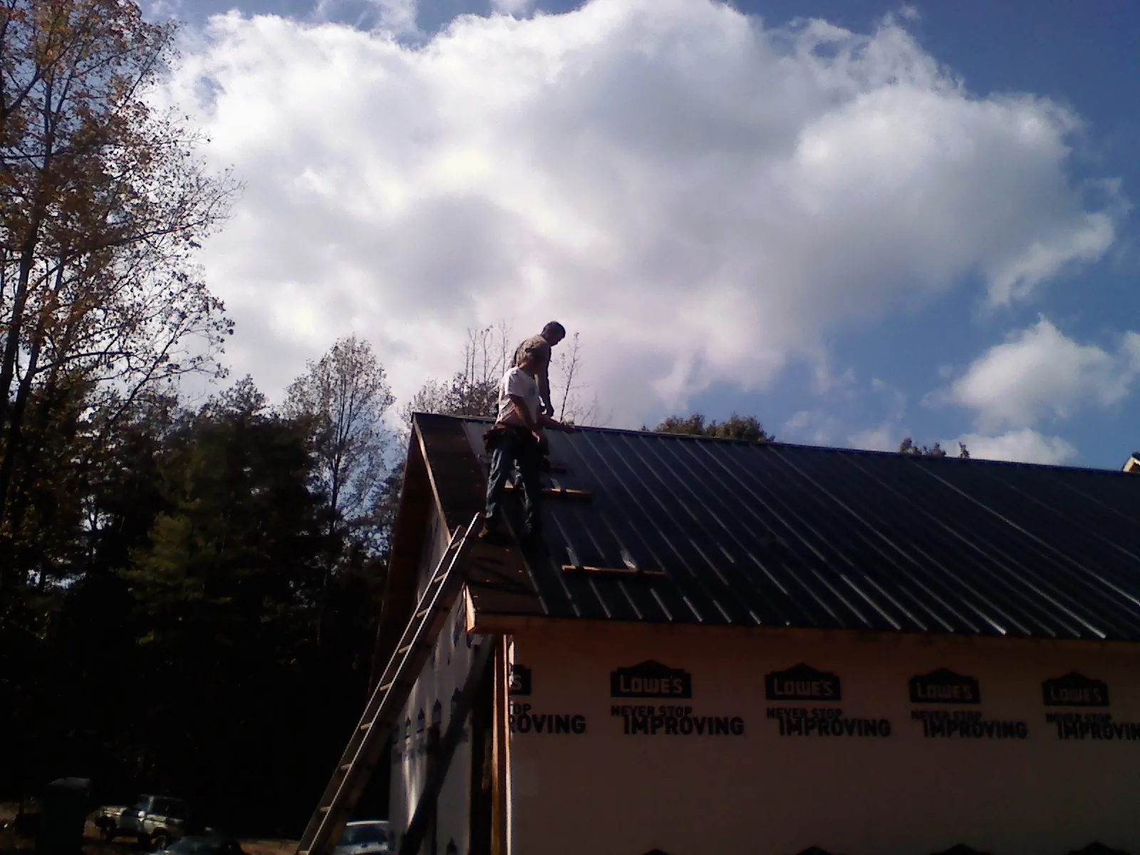 Roofer fastening dark metal panels high against a cloudy sky, from a Roof Inspection job in Fitzwilliam