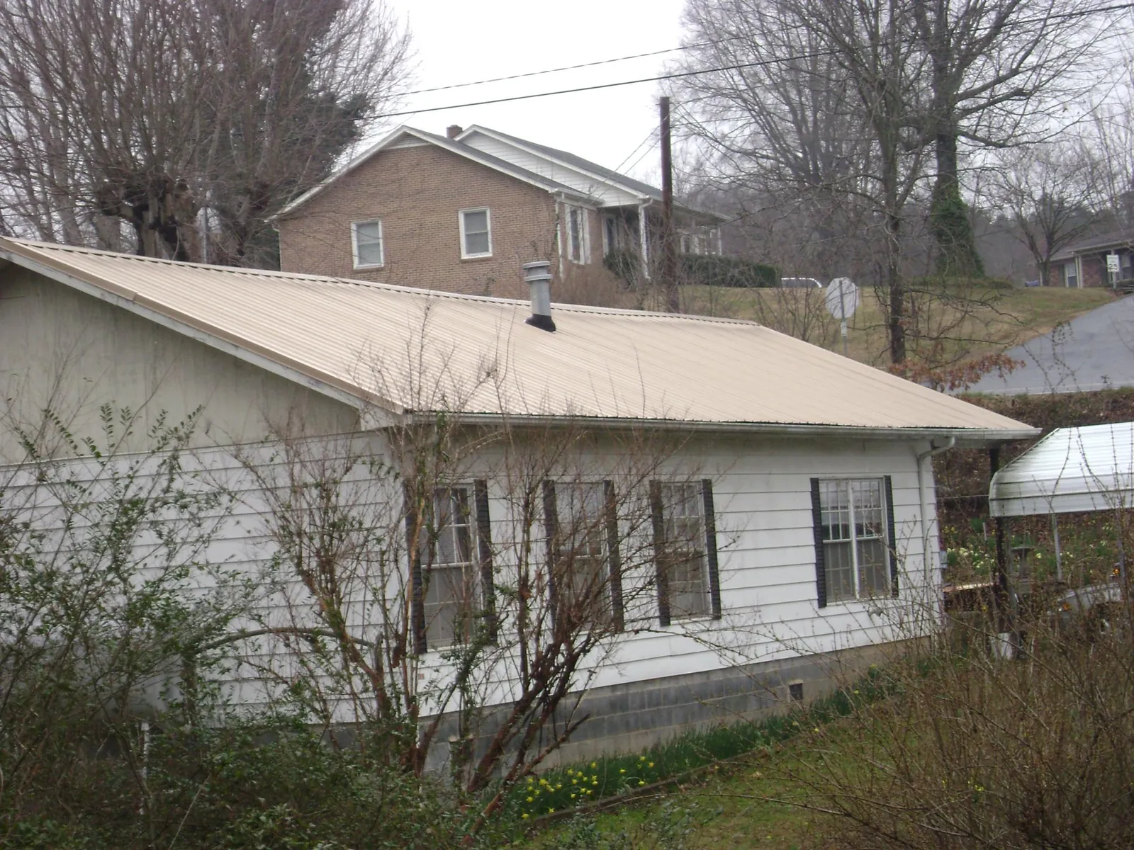 Tan metal roof on a white sided house set into a hillside — Commercial Roofing by Roofing Brothers in Fitzwilliam